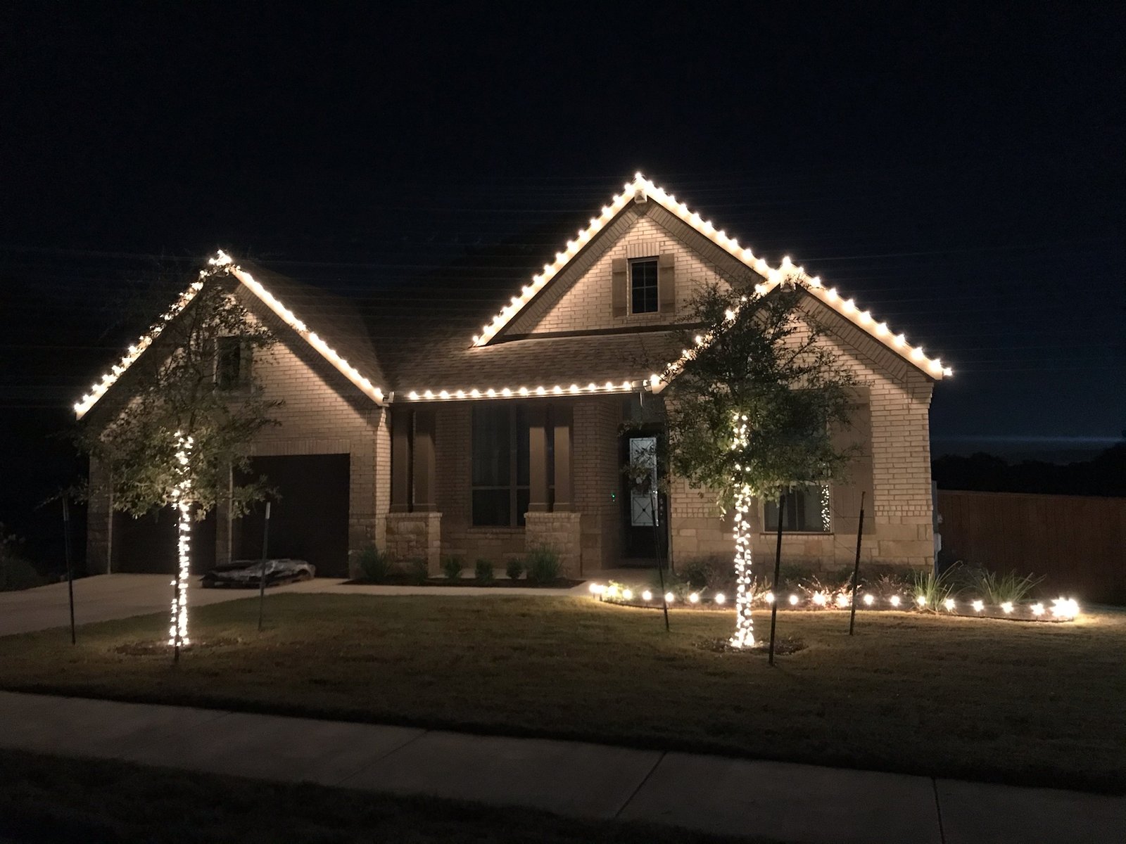 Warm white Christmas roofline and tree lighting installation on a Texas home